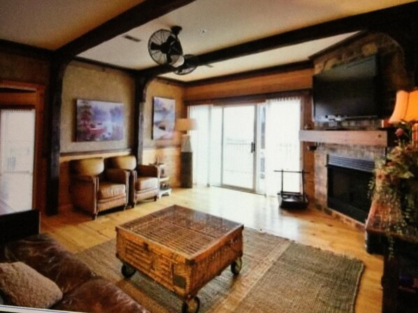 A spacious living room with a large wooden coffee table, a fireplace, and a television mounted on the wall.