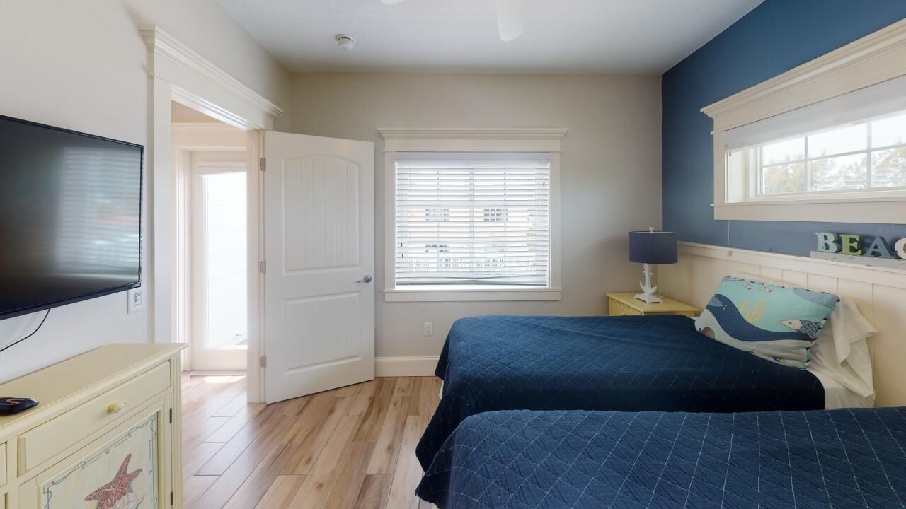 Une chambre avec deux lits, une télévision, une fenêtre avec des stores et une commode.