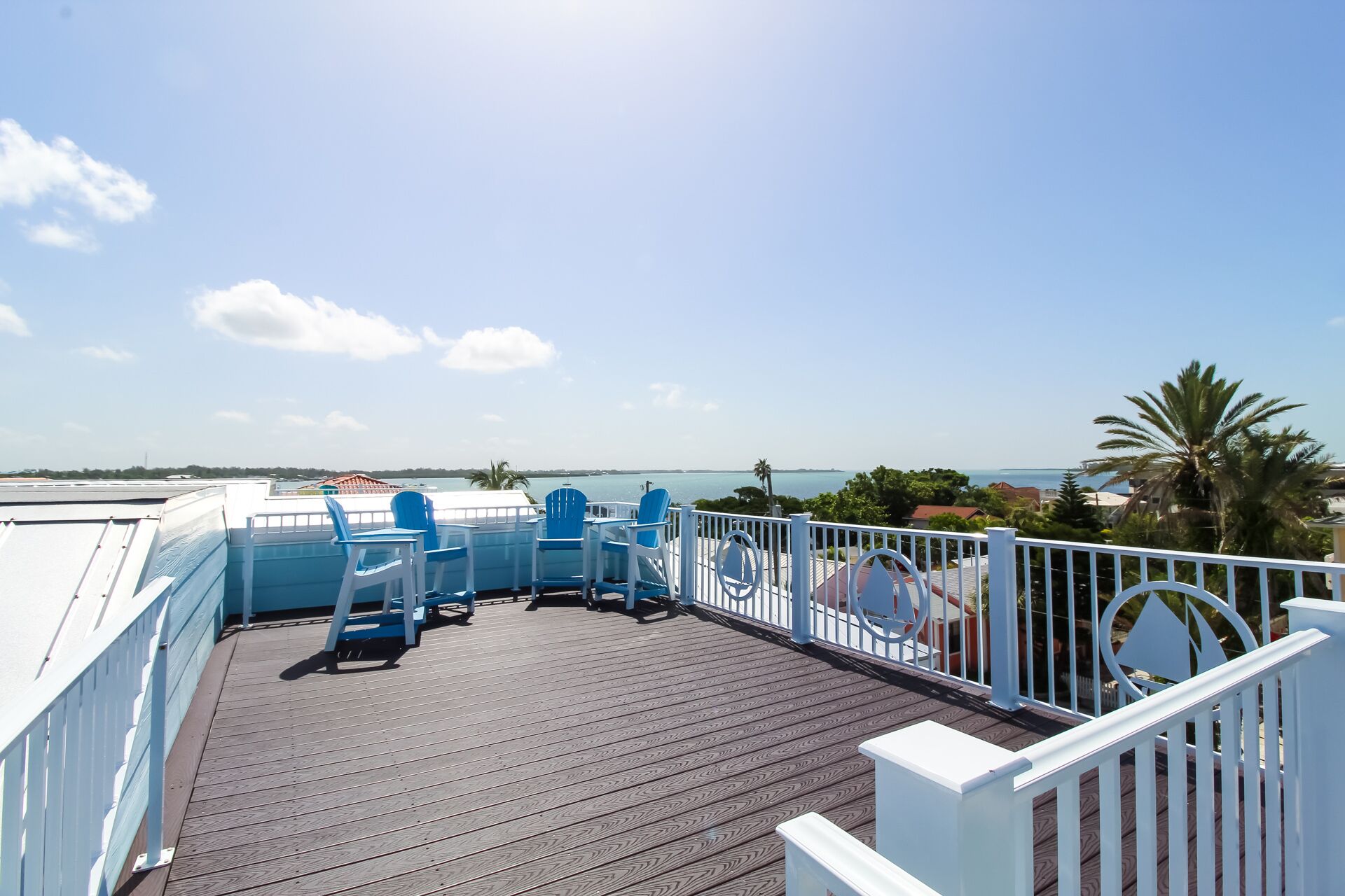 Een houten terras met blauwe stoelen en een witte balustrade met uitzicht op het water.