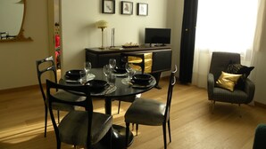 Un coin repas avec une table ronde, des chaises noires et un téléviseur posé sur un meuble.