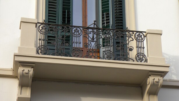 Un balcon orné de balustrades en métal ouvragé et de volets verts.