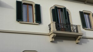 Une façade d’immeuble avec trois fenêtres, chacune dotée de volets verts et d’un balcon orné de balustrades en fer forgé.