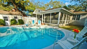 A swimming pool with lounge chairs, a covered patio, and a fenced backyard. - Patti's 1625 Bungalow | East Beach St. Simons Island Cottage with Pool (Saint Simons Island)