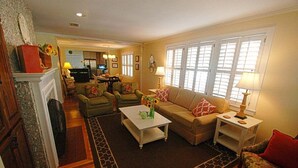 A living room with a fireplace, a sofa set, a coffee table, and a television in the background. - Patti's 1625 Bungalow | East Beach St. Simons Island Cottage with Pool (Saint Simons Island)