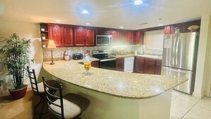 Una cocina con encimeras de granito, armarios de madera, microondas integrado, refrigerador y una isla central con taburetes de bar.