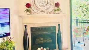 Una sala de estar con chimenea, ventilador de techo y televisor sobre un mueble.