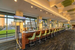 A modern bar area with a long counter, multiple bar stools, and large windows offering a view of the cityscape.