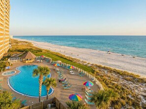 A resort pool area with a circular pool, lounge chairs, umbrellas, and a beach view.