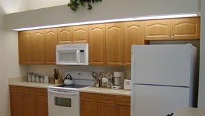 A kitchen with wooden cabinets, a microwave, a stove, a refrigerator, and a countertop with various kitchen items. - Luxury Villa on main Rotonda canal (Rotonda West)
