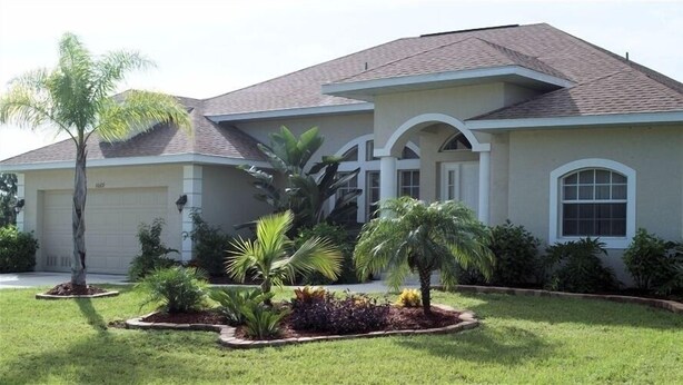 A residential house with a garage, a well-maintained lawn, and various tropical plants. - Luxury Villa on main Rotonda canal (Rotonda West)