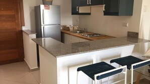 A compact kitchen with a built-in refrigerator, a sink, and a bar area with stools.