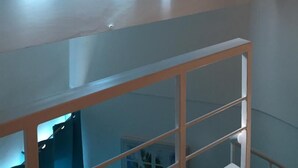A bunk bed with a white frame and a lower bunk with a wooden ladder. There is a red pendant light hanging from the ceiling.