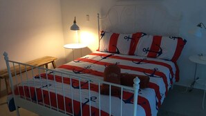 A bed with a white metal frame, a red and white striped bedspread, and matching pillows. There is a small bedside table with a lamp.
