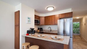 Una cocina moderna con armarios de madera, un refrigerador de acero inoxidable, un microondas y una cafetera. Hay tres taburetes de madera en la isla.