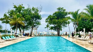 A rectangular swimming pool with clear blue water, surrounded by lounge chairs and palm trees.