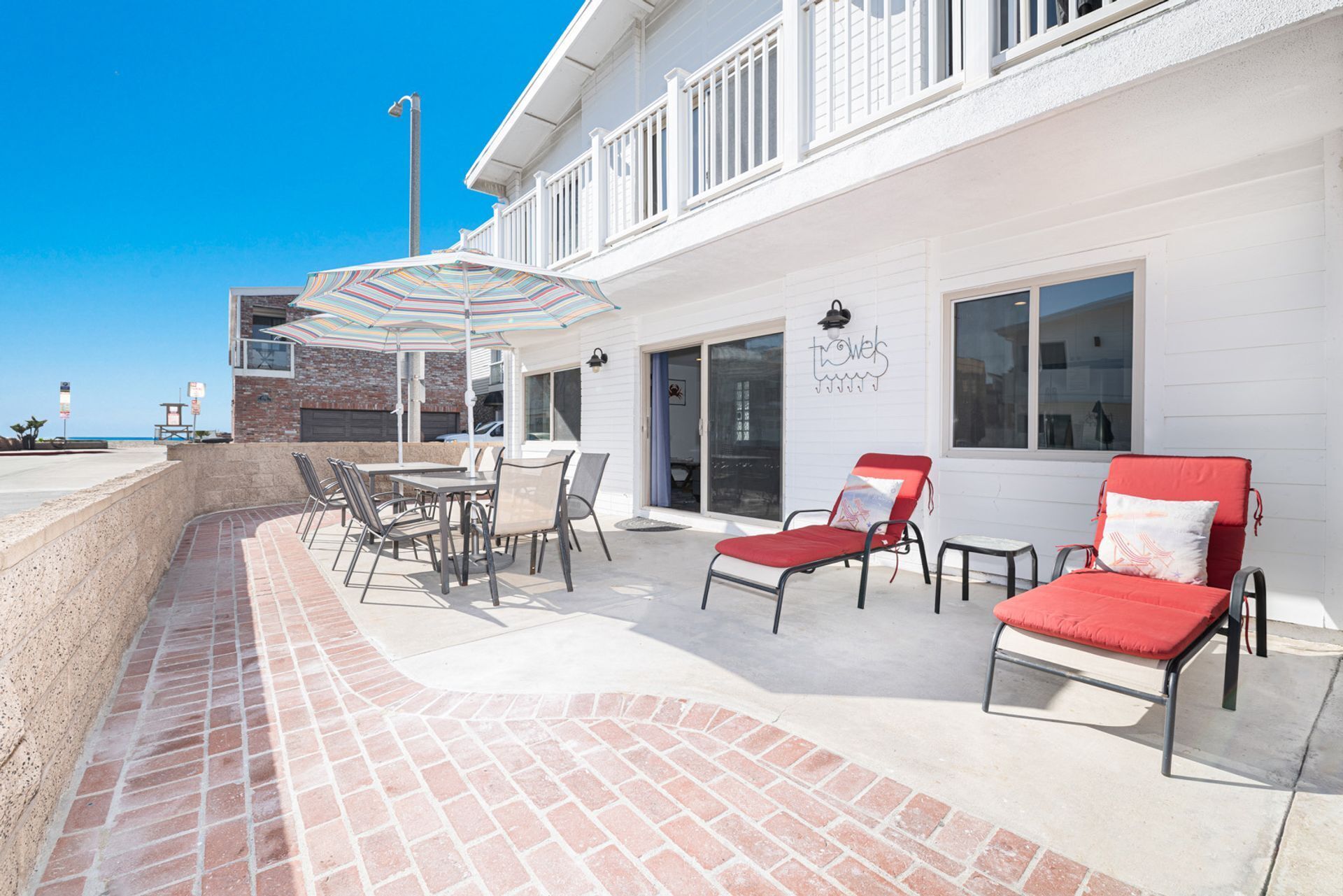 An outdoor patio with a brick floor, a table with chairs, and two red lounge chairs.