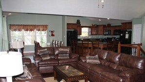 A spacious living room with leather sofas, a coffee table, and a dining area with wooden chairs and a kitchen in the background. - Super Location in Lakeside Estates--w/pool; basketball ct; walking tr; boat ramp (Lafollette)
