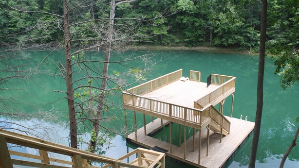 A wooden deck with a table and chairs overlooking a calm body of water surrounded by trees. - Super Location in Lakeside Estates--w/pool; basketball ct; walking tr; boat ramp (Lafollette)