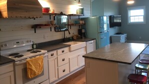 A kitchen with white cabinets, a stove, a sink, and a refrigerator. There are hanging lights and a window. - Relax At The Farm!   Newly Built Studio Apartment In The Barn At Selah Farm (Kalispell)