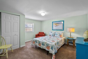 A bedroom with a bed, a chair, a desk, a lamp, and a door. - "Sand Dollar Suites" suite 1: A short stroll from our sandy shores! (Carolina Beach)