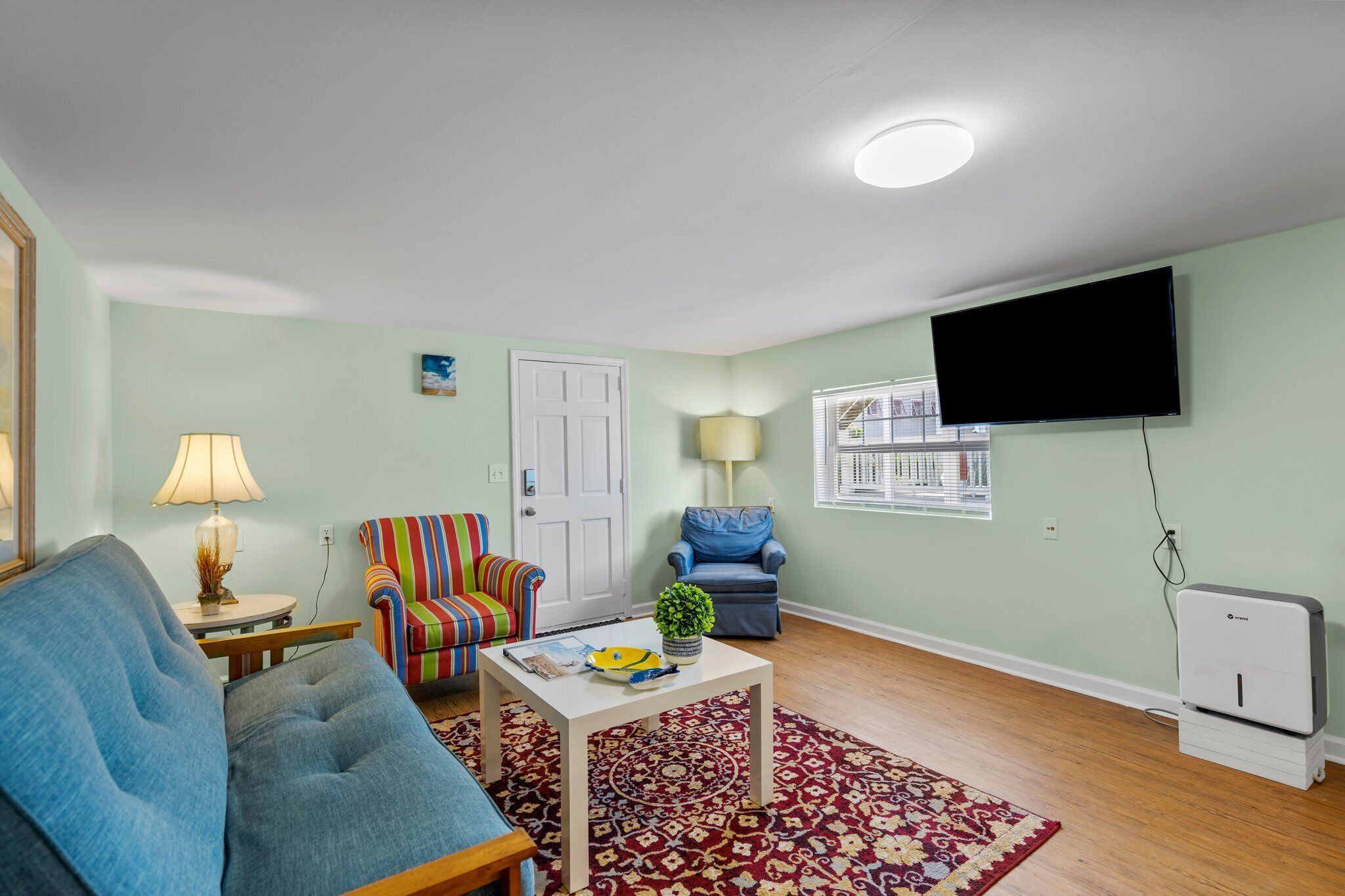 A living room with a blue sofa, a striped armchair, a small coffee table, a lamp, a television, and a heater.