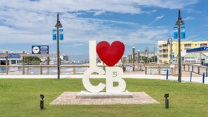 A public space with a large heart-shaped sculpture, a waterfront view, and a boardwalk with shops. - "Sand Dollar Suites" suite 1: A short stroll from our sandy shores! (Carolina Beach)