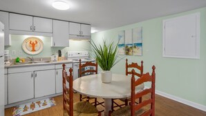 A kitchen with white cabinets, a stove, and a sink. There is a dining table with chairs and a potted plant. - "Sand Dollar Suites" suite 1: A short stroll from our sandy shores! (Carolina Beach)