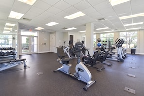 Ein Fitnessstudio mit verschiedenen Cardiogeräten, Gewichtsbänken und Hanteln.