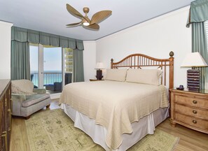 A hotel room with a bed, a chair, a nightstand, a lamp, a ceiling fan, and a view of the ocean. - Spacious 3-bed, 3-bath beachfront end unit w/ balcony! 🌊 (Destin)