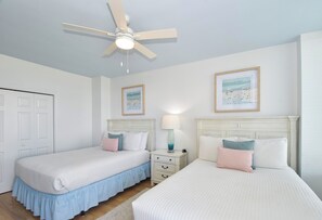 A bedroom with two beds, a ceiling fan, a nightstand with a lamp, and two framed pictures on the wall. - Spacious 3-bed, 3-bath beachfront end unit w/ balcony! 🌊 (Destin)