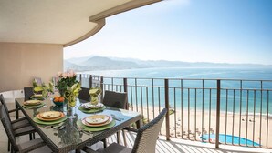 Varanda com mesa de jantar posta para dois, com vista para a praia e o mar.