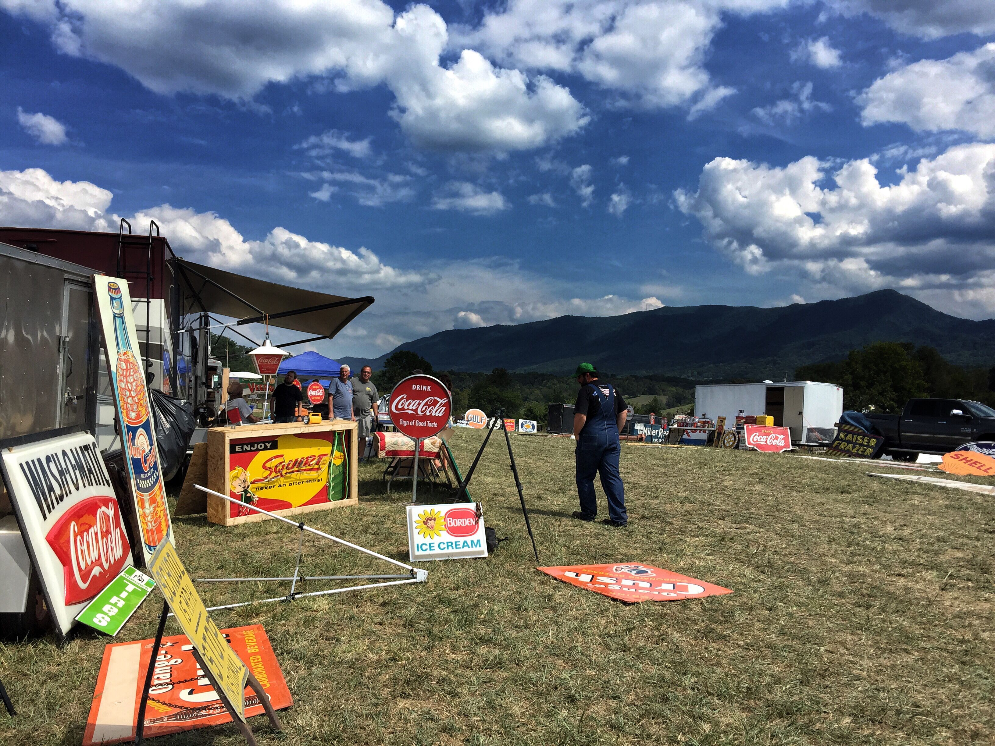 A food truck area with various food and drink signs, a tent, and a mountainous backdrop.