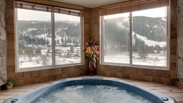 A room with a hot tub, large windows with a snowy landscape view, and a vase with flowers. - Large 3 BR/3 BA Near Mountain House Lifts; Private Hot Tub in unit; 7 beds (Keystone)