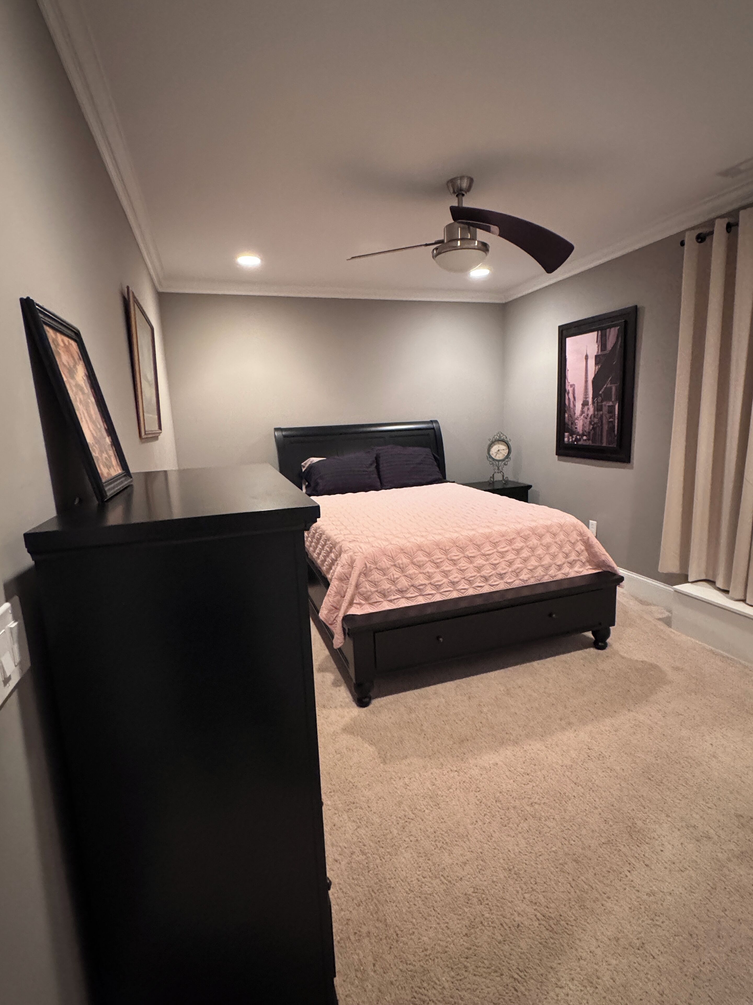 Un dormitorio con cama, cómoda, ventilador de techo y un cuadro en la pared.