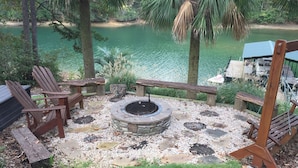 Een terras met Adirondack-stoelen, een vuurkorf van steen en uitzicht op een meer.