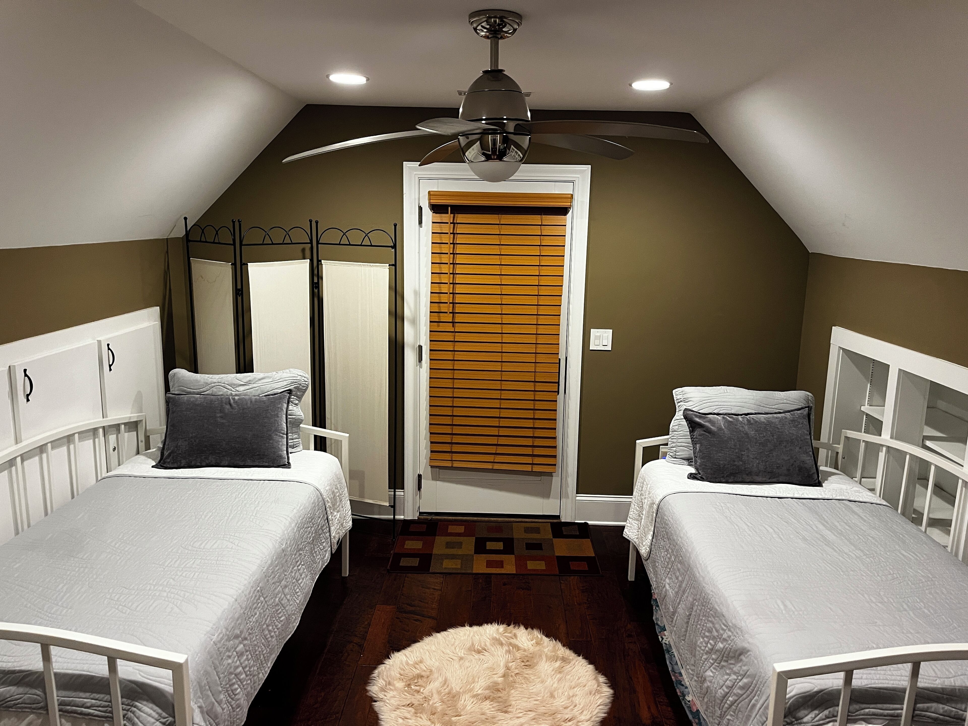 Une chambre avec deux lits simples, un ventilateur de plafond et une porte avec des stores.