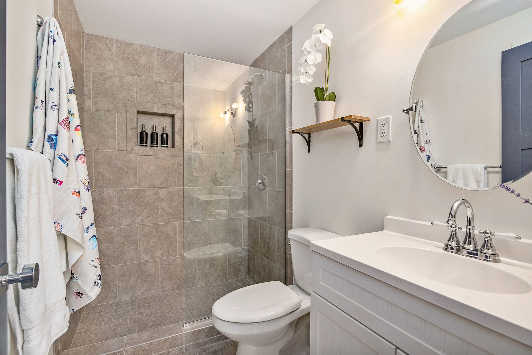 A bathroom with a shower, toilet, sink, and a mirror.