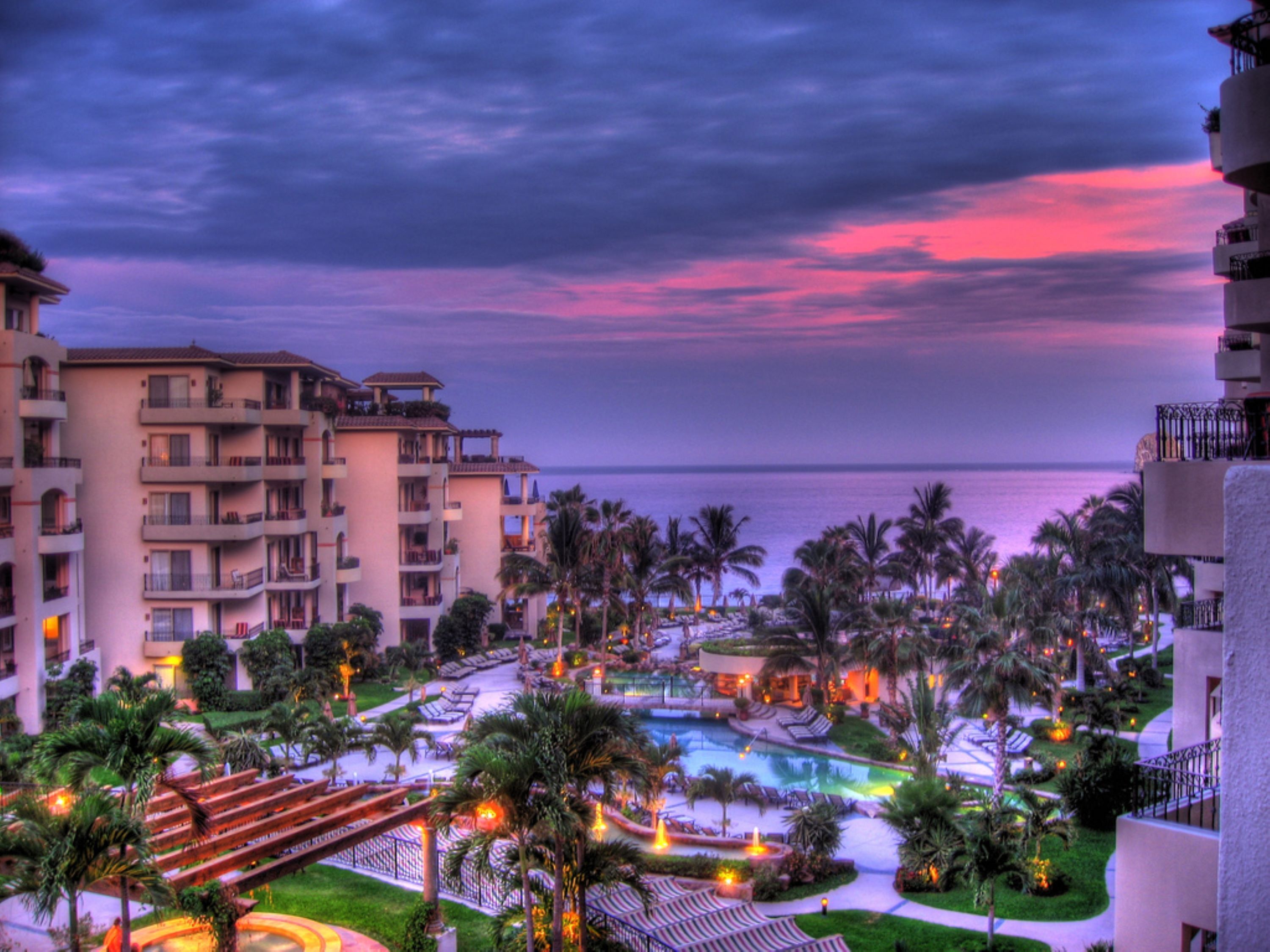 A resort with multiple buildings, a swimming pool, and palm trees.