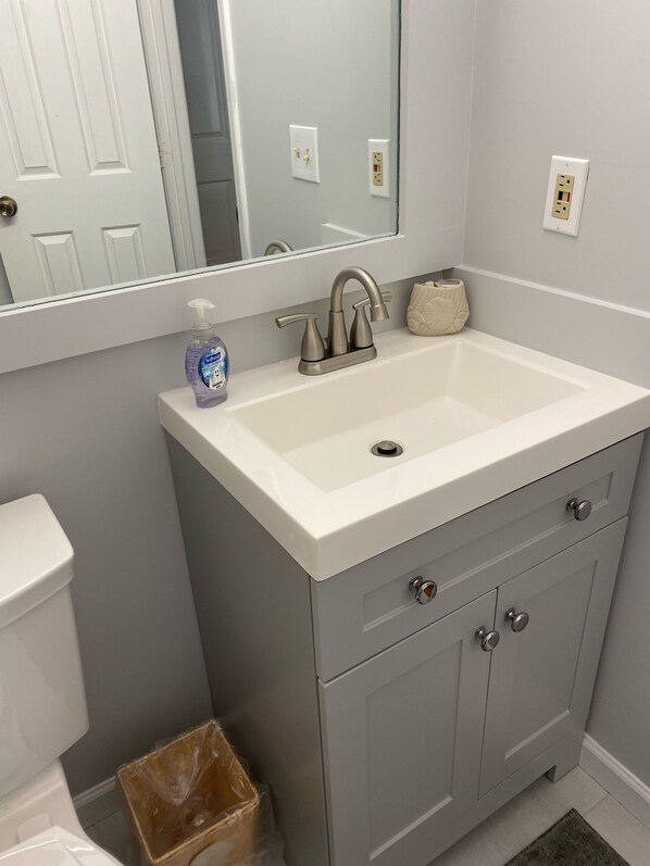 A bathroom with a white sink, a mirror, a toilet, and a trash bin.