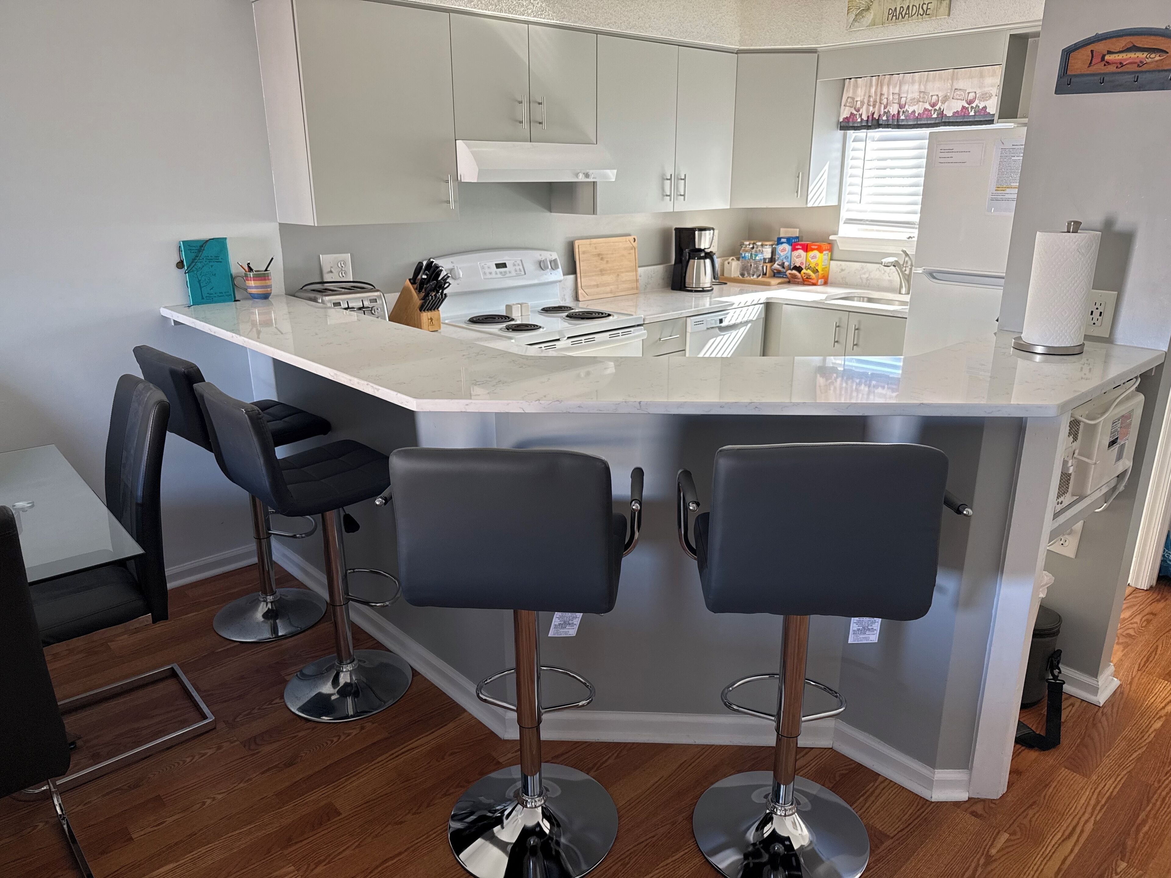 Une cuisine moderne dotée d’un îlot central, de deux tabourets de bar, d’une table à manger et d’un petit coin salon.