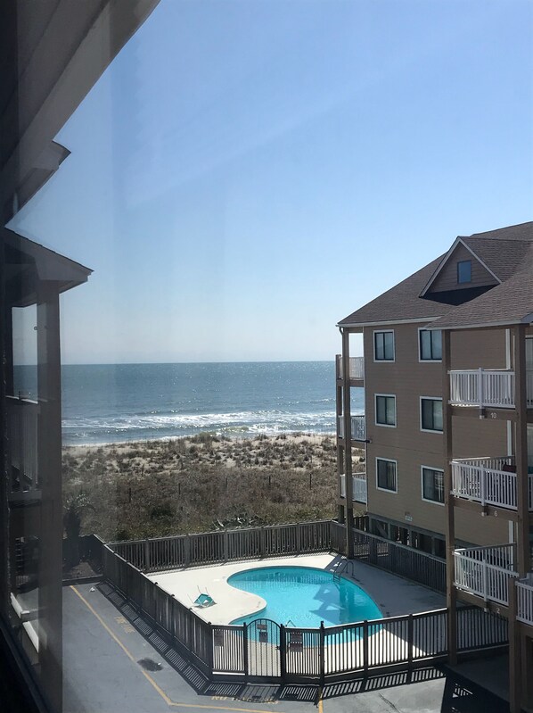 Blick auf ein Schwimmbecken mit Strand und Meer im Hintergrund.
