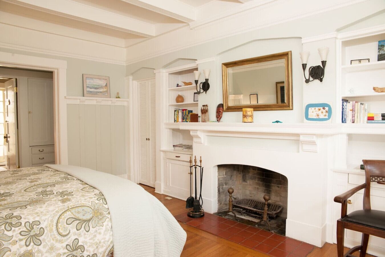 A bedroom with a bed, a fireplace, a bookshelf, and a mirror.