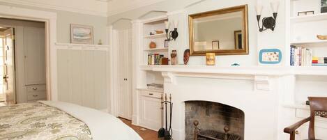 A bedroom with a bed, a fireplace, a bookshelf, and a mirror.