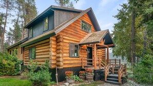 A log cabin with a porch, stone steps, and a view of the surrounding forest.