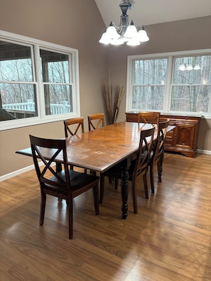 Une salle à manger avec une table et des chaises en bois, de grandes fenêtres et un lustre.