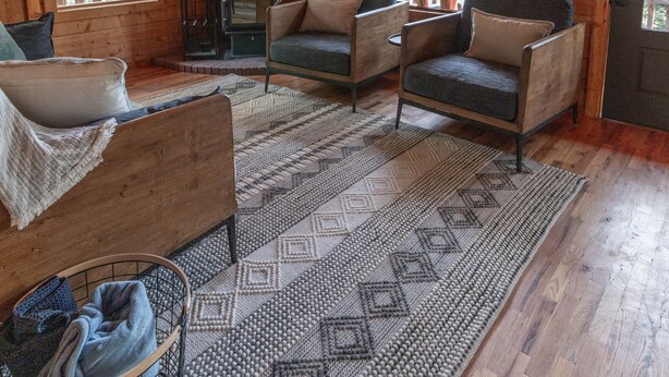 L’intérieur d’un chalet accueillant, avec des murs en bois, une cheminée, un canapé et un tapis à motifs.