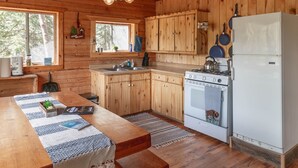Une cuisine rustique aménagée dans une cabane en bois, avec une grande table en bois, un poêle, un évier et des placards en bois.