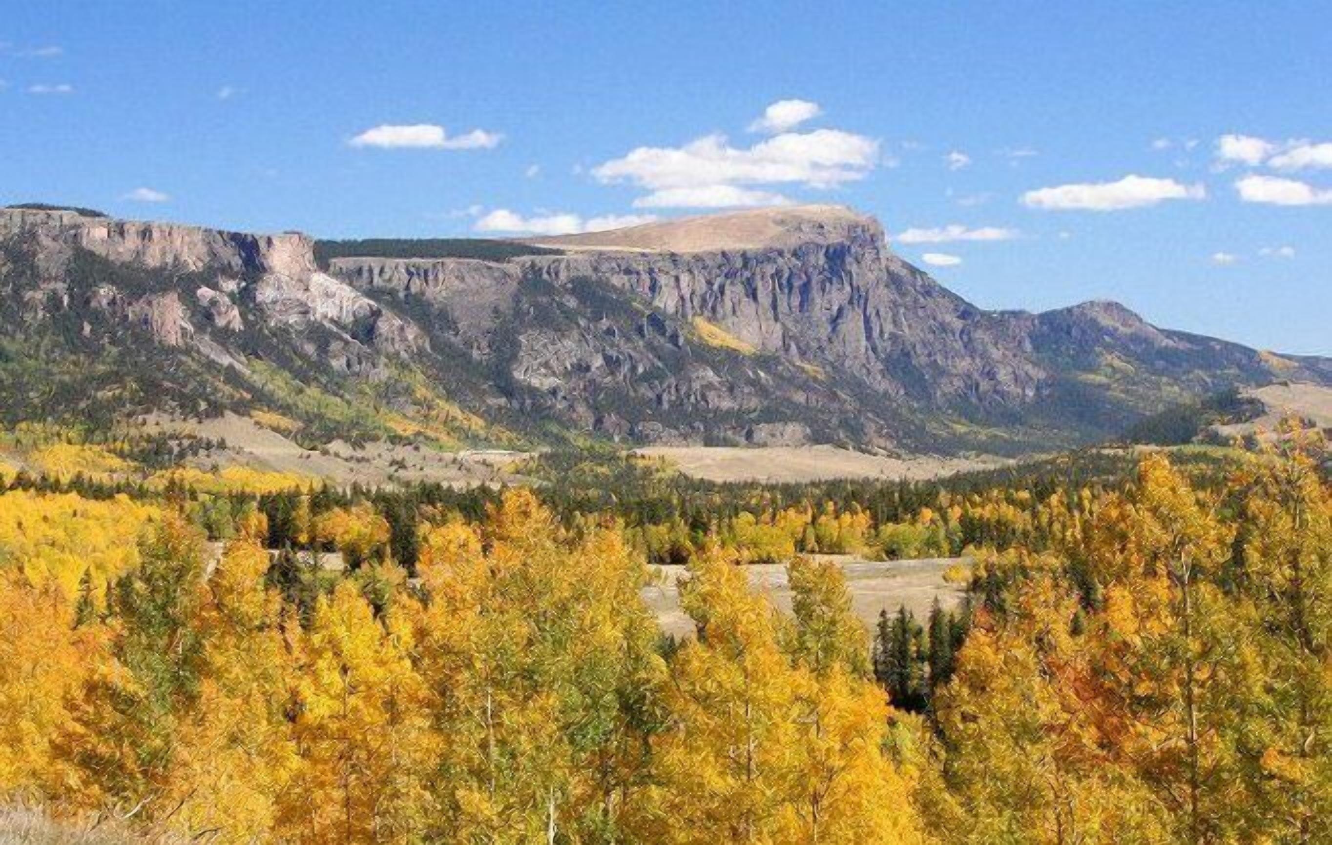 Un paysage montagneux aux couleurs automnales, sous un ciel dégagé.