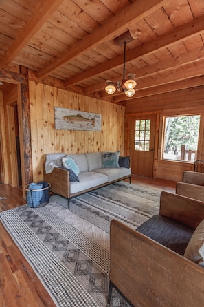 Interior acogedor de una cabaña con techo de madera, un sofá con cojines, un tapete estampado y un banco de madera.
