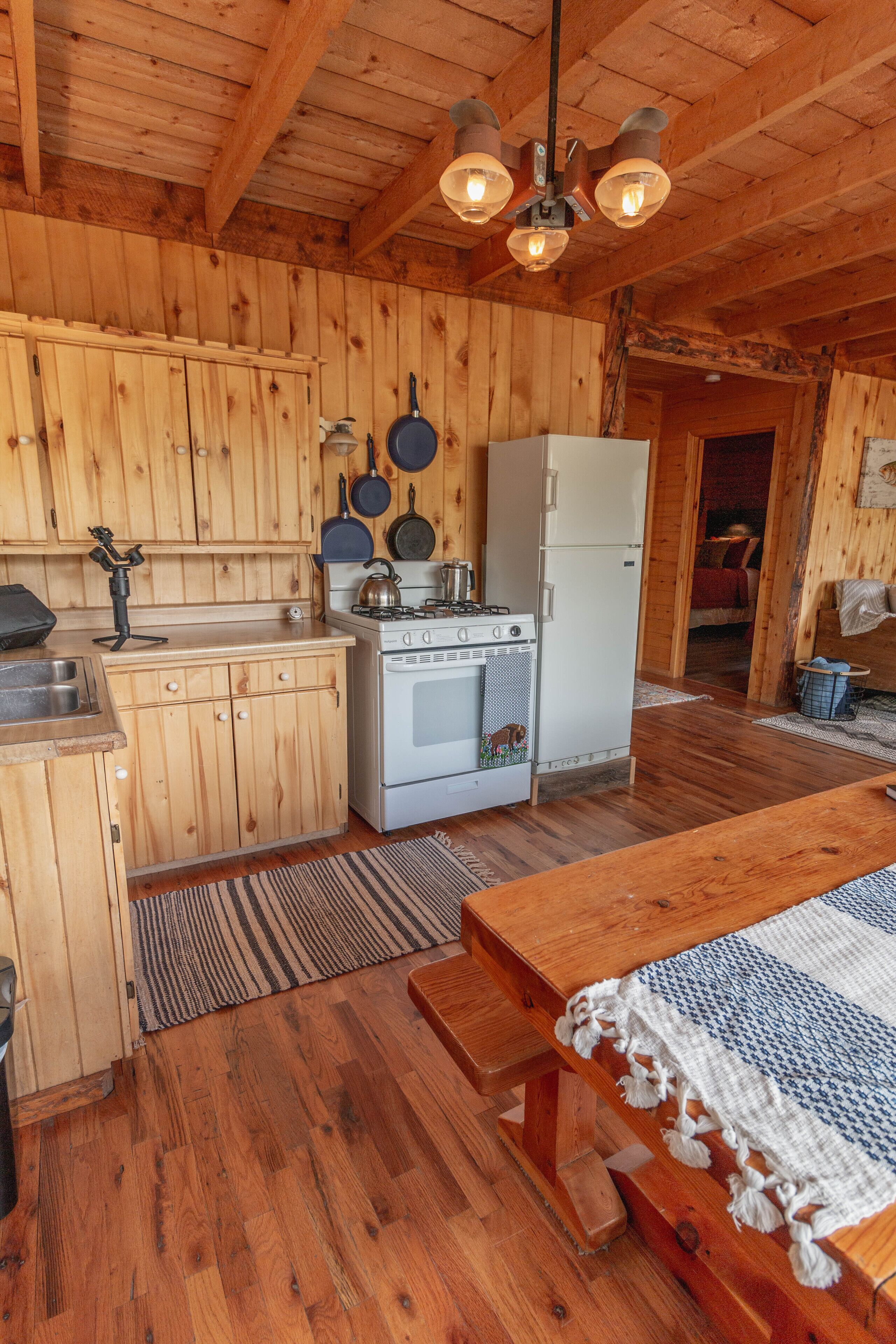 Cocina de madera rústica con estufa, refrigerador y ollas colgantes.